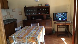A small kitchen with a dining table, chairs, a television, and a clock on the wall. - Sunny apartment in a residential area, not far from the historic center (Pisa)