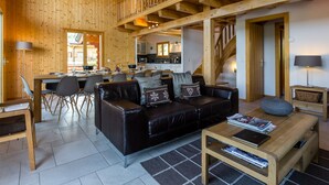 A spacious living area with a wooden ceiling, a black leather sofa, a dining table, and a kitchen in the background. - Chalet le Fauconnier - La Tzoumaz, 4 Vallees (La Tzoumaz)