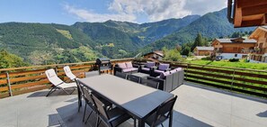 Een terras met een tafel, stoelen, een barbecue en uitzicht op bergen.