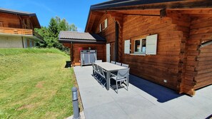 Een houten chalet met een patio, inclusief een tafel, stoelen en een klein zitje buiten.