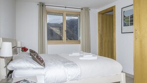 A neatly made bed with white linens, a bedside table with a lamp, and a window with curtains. - Chalet le Fauconnier - La Tzoumaz, 4 Vallees (La Tzoumaz)