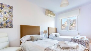 Hotellihuone, jossa on kaksi sänkyä, valkoinen tuoli, lamppu ja ikkuna, josta on näkymä rakennuksiin.