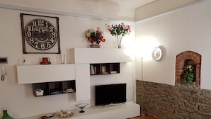 A living room with a flat-screen TV, white shelving, a brick fireplace, and a green sofa.