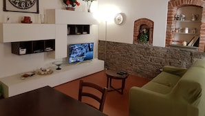 A living room with a television, a brick fireplace, a green sofa, and a dining table.