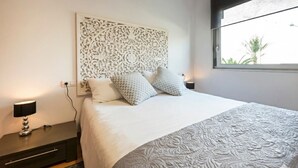 Een keurig opgemaakt slaapkamer met een groot bed, een decoratief hoofdbord, bedlampjes en een raam met uitzicht.
