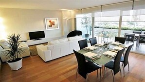 Een moderne woonkamer met een glazen eettafel, witte banken en een flatscreen-televisie.