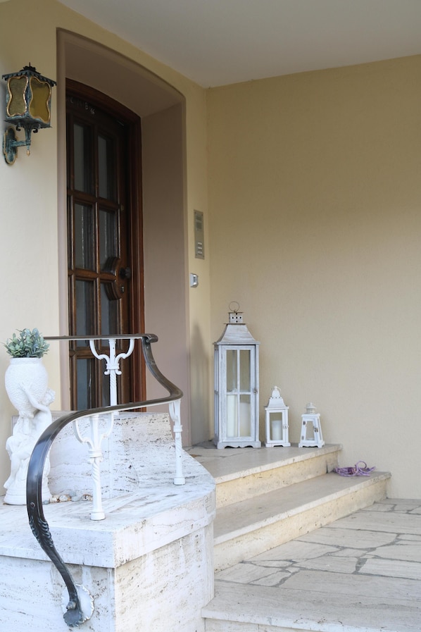 A stone staircase leading to a wooden door, with a white railing and a small potted plant on the left.