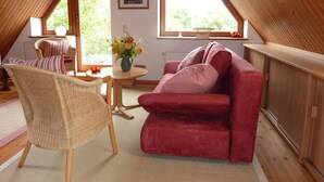 A cozy attic room with a red sofa, wicker chair, and a table with a vase of flowers. - Garden idyll at the Wadden Sea National Park (Wesselburen)
