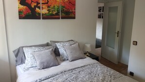 Une chambre à coucher avec un lit, des oreillers, une table de chevet, une lampe et un tableau accroché au mur.