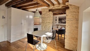 Una cocina moderna con armarios blancos, una mesa de comedor redonda y sillas negras. Se aprecia una pared de piedra y vigas de madera en el techo.