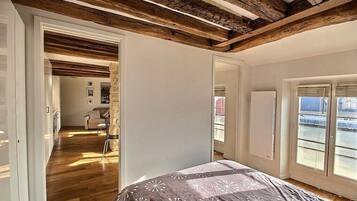 Une chambre avec un plafond en bois, un lit recouvert d’une couvre-lit à motifs, une fenêtre donnant sur un paysage agréable et une porte menant à une autre pièce.