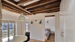Una habitación con vigas de madera a la vista, una mesa blanca con una silla negra y una cama con colcha estampada.