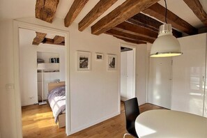Una habitación con vigas de madera, una cama, una mesa blanca y una lámpara colgante.