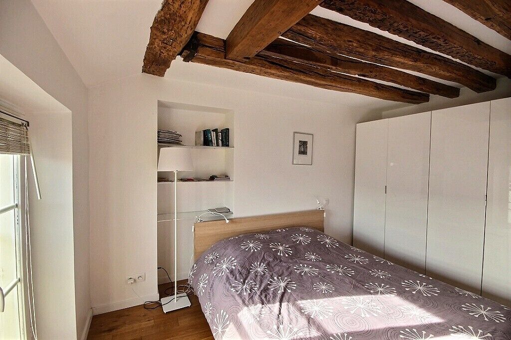A bedroom with a bed, a wardrobe, a shelf unit, and a window.