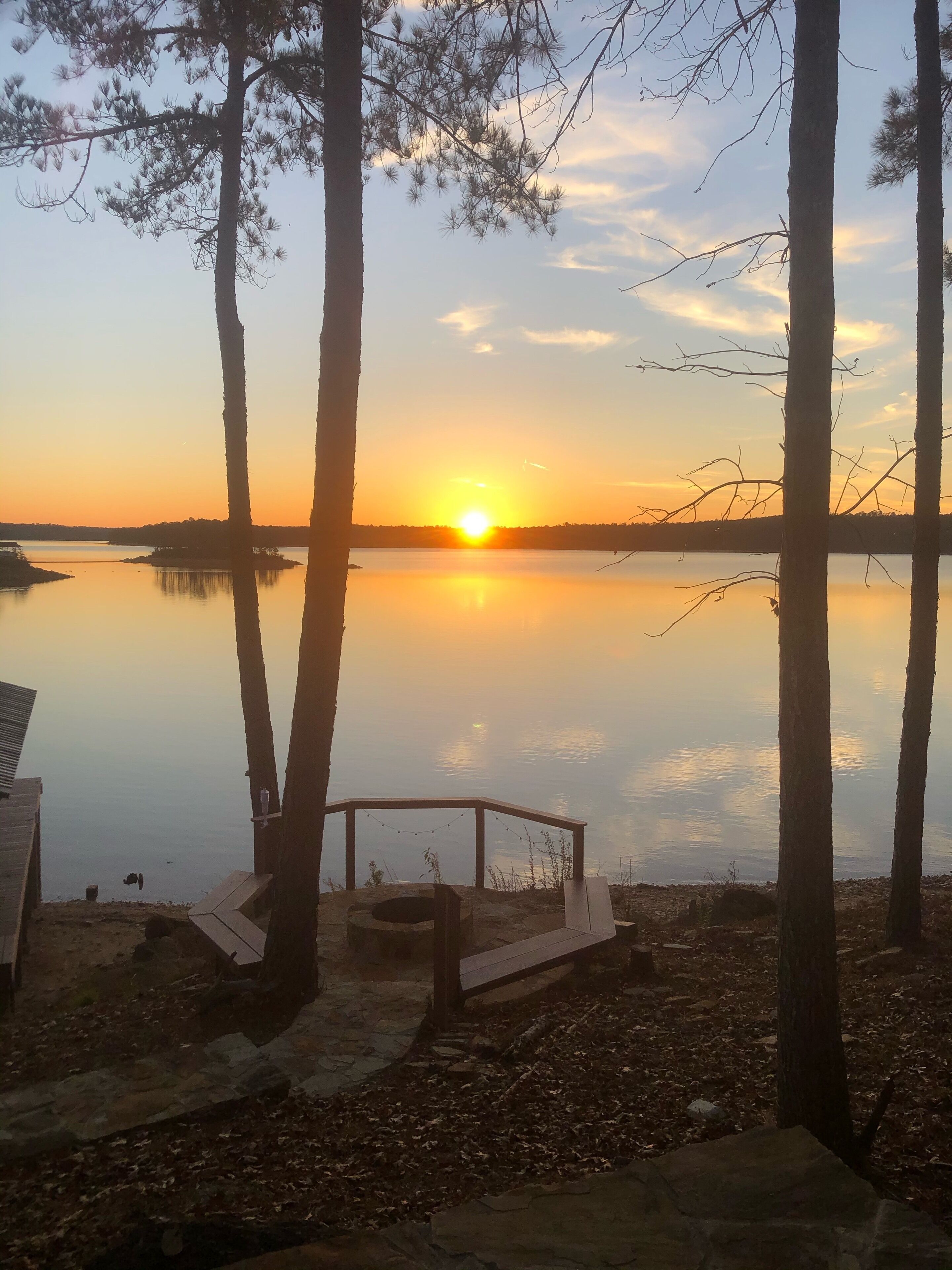 A serene lakeside view with a sunset, surrounded by trees and a wooden structure with a bench.