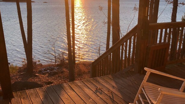 A wooden deck with a rocking chair, overlooking a body of water with trees and a distant shoreline.