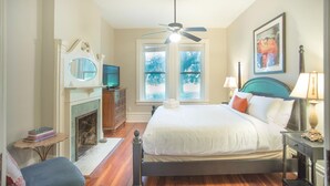 Quarto com cama, ventilador de teto, lareira, televisão e janela com vista para árvores.