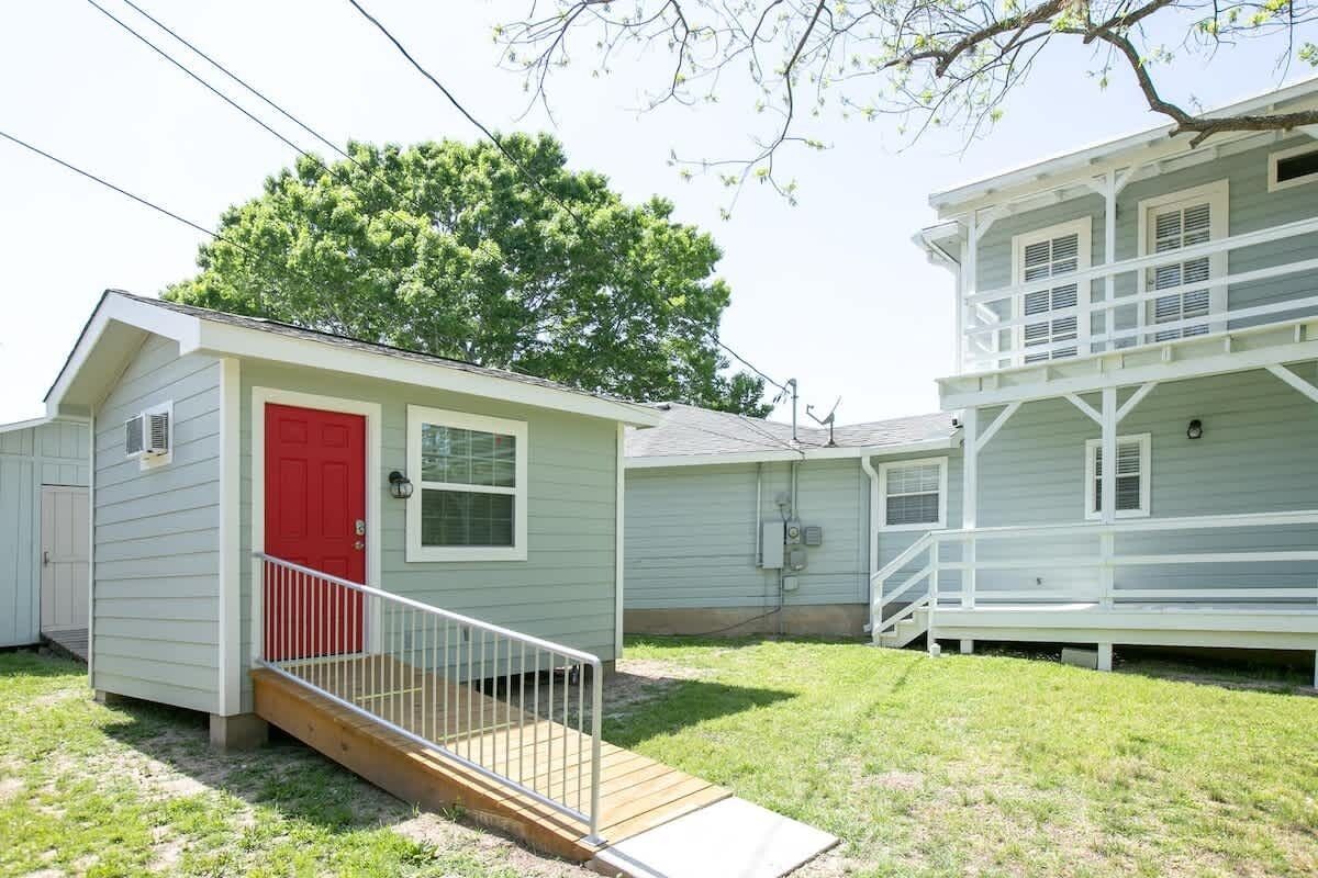 A small, single-story house with a red door and a wooden front porch.