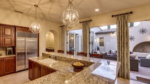 A kitchen with granite countertops, a stainless steel refrigerator, and a hanging light fixture. - Cappella - Gorgeous 4 br Villa in PGA West with Pool/Spa + Golf Course Views #259222 (La Quinta)