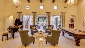 A spacious living room with a grand piano, comfortable seating, a pool table, and a view of a staircase leading to outdoor areas. - Cappella - Gorgeous 4 br Villa in PGA West with Pool/Spa + Golf Course Views #259222 (La Quinta)
