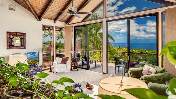 A spacious living area with a large sliding glass door leading to a balcony with a view of palm trees and the ocean.