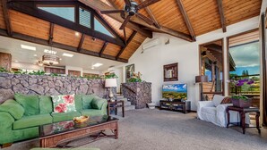 A spacious living room with a high ceiling, stone wall, and large windows.