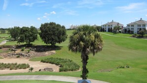 Un campo de golf con cielo despejado, una palmera y un edificio de varios pisos al fondo.