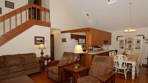A spacious living room with a wooden staircase, a dining area with white chairs, and a kitchen with wooden cabinets. - 3 Bedroom 2 bath Home, Easy Access, Covered Porch, Diligent Views & Internet (Maggie Valley)