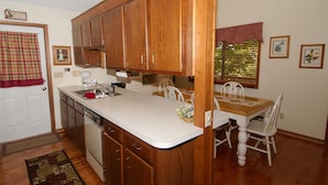 A kitchen with wooden cabinets, a white countertop, a sink, and a dining area with a table and chairs. - 3 Bedroom 2 bath Home, Easy Access, Covered Porch, Diligent Views & Internet (Maggie Valley)