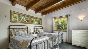 Une chambre avec deux lits, une commode et une fenêtre donnant sur des arbres.