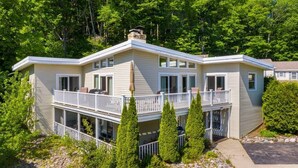 Une maison à deux étages avec un balcon, entourée d’arbres et bordée d’un terrain rocheux.