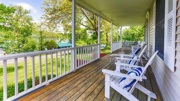 Une véranda couverte avec des balustrades blanches et un plancher en bois, agrémentée de plusieurs fauteuils blancs dotés de coussins bleus.