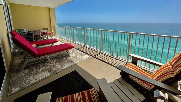 Un balcon avec vue sur l’océan, des fauteuils rouges et une table agrémentée de coussins à rayures.