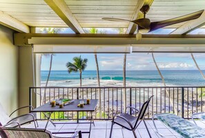 A balcony with a table and chairs, overlooking a beach with palm trees and the ocean. - Kona Bali Kai 317 Direct Oceanfront, Major Upgrade with Central Air. (Kailua Kona)