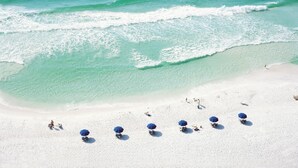 Een strand met helder turquoise water en wit zand. Er staan verschillende blauwe parasols en ligbedden.