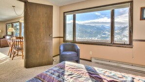 Une chambre avec une grande fenêtre, un lit, une chaise et une vue sur les montagnes.