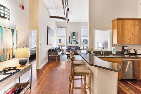 A modern kitchen with a built-in dishwasher, wooden cabinets, and a granite countertop. - Contemporary Living on Broughton with King Beds & Parking by Lucky Savannah (Savannah)