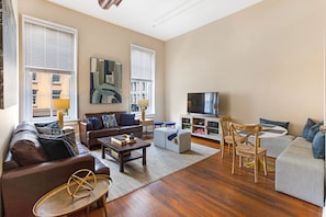 A living room with a brown leather sofa, a grey sofa, a wooden coffee table, and a TV on a stand.