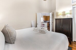 Ein Hotelzimmer mit Bett, Kissen und Handtüchern. Im Hintergrund sind ein Kleiderschrank und eine Küche zu sehen.