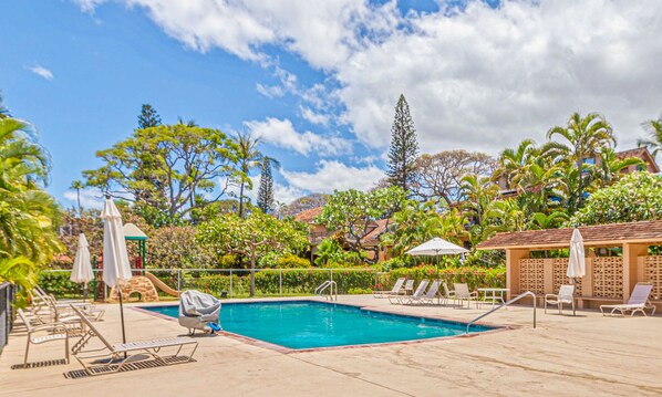 A pool area with lounge chairs and umbrellas, surrounded by tropical vegetation and a clear sky. - Location, Location.... Just Steps Away from the Ocean! (Lahaina)