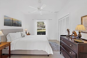 A bedroom with a bed, a nightstand, a dresser, a ceiling fan, and a window with curtains. - Serene Waterfront Home | Pool, Spa, & Water View (Marco Island)
