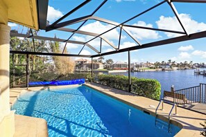 An outdoor swimming pool with a view of a body of water and palm trees. - Serene Waterfront Home | Pool, Spa, & Water View (Marco Island)