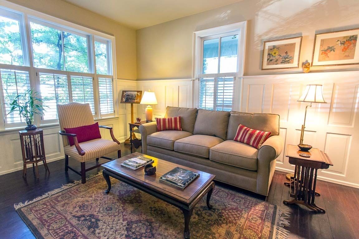 A living room with a beige sofa, a striped armchair, a coffee table, and a patterned rug.