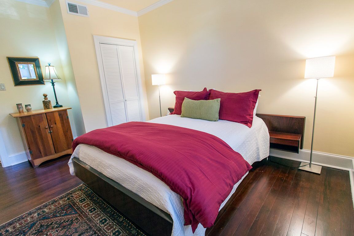 A bedroom with a large bed, a wooden nightstand, a bedside table, a floor lamp, and a door.