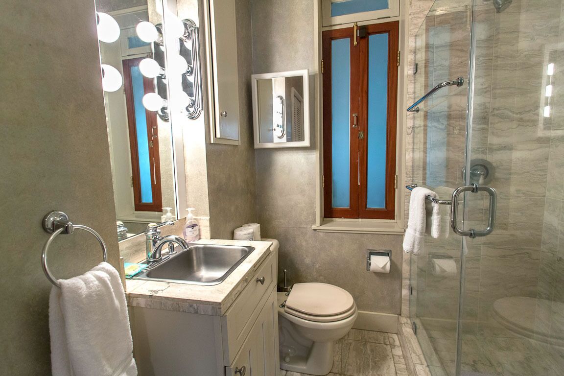 Un baño con lavamanos, espejo, tocador, inodoro y zona de ducha con mampara de vidrio.