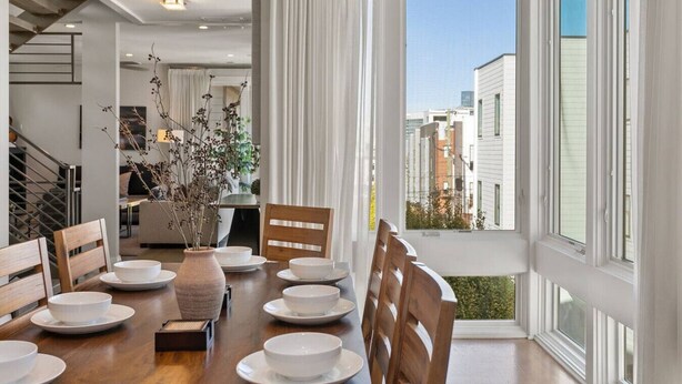 Un comedor con mesa de madera dispuesta para cuatro personas, platos blancos y un jarrón con flores secas.