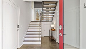 Una escalera moderna con barandilla de vidrio, paredes blancas y una puerta roja.
