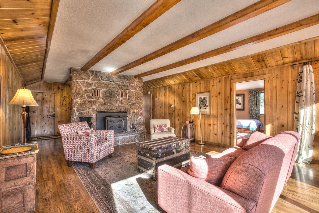 A cozy room with a stone fireplace, wooden beams, a patterned sofa, and a rustic wooden floor.