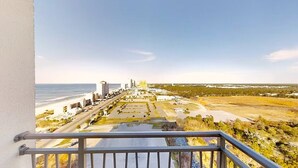 Un balcón con vista a la costa, que incluye una playa, un estacionamiento y edificios.