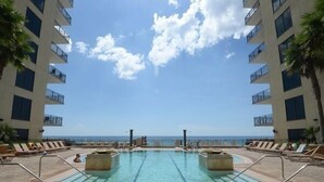 Zona de piscina con agua cristalina, sillas de descanso y vista al océano.